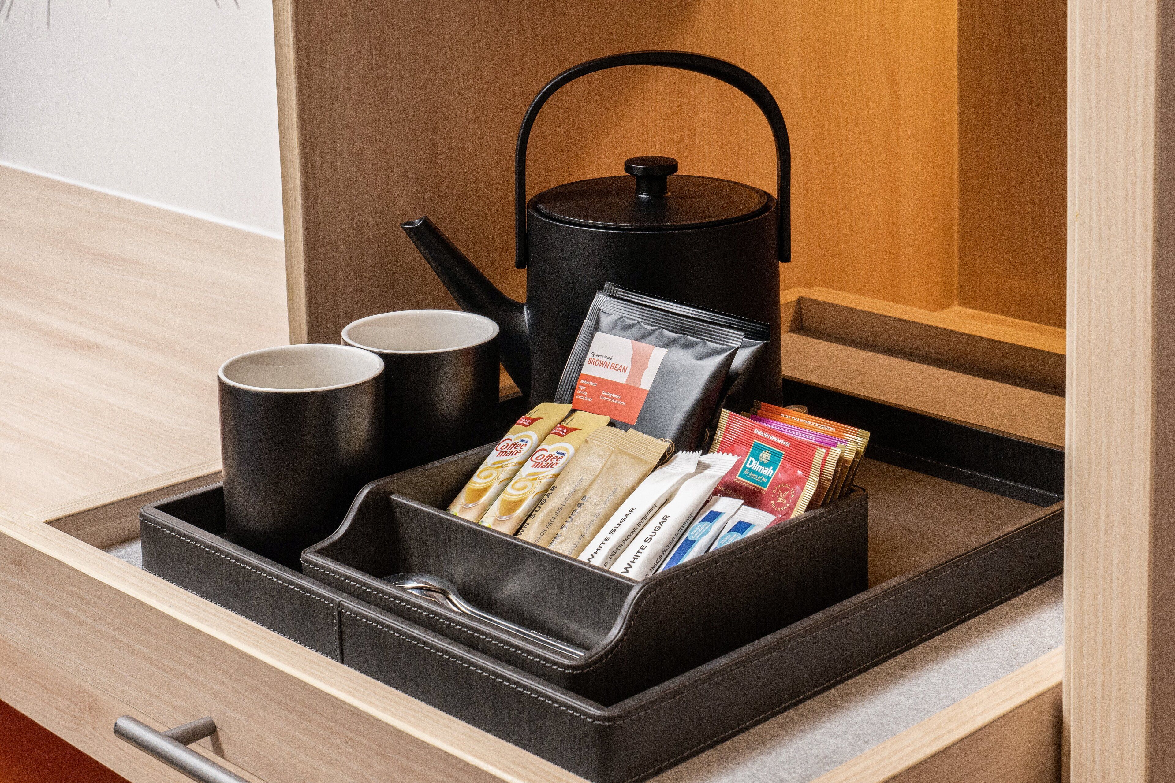 A drawer with a tea kettle, two cups, and various coffee and tea packets.