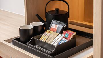 A drawer with a tea kettle, two cups, and various coffee and tea packets.