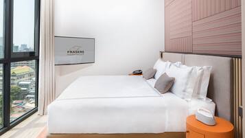 Una habitación de hotel moderna con una cama grande, una mesita de noche, un cartel enmarcado en la pared y vistas de la ciudad a través de amplios ventanales.