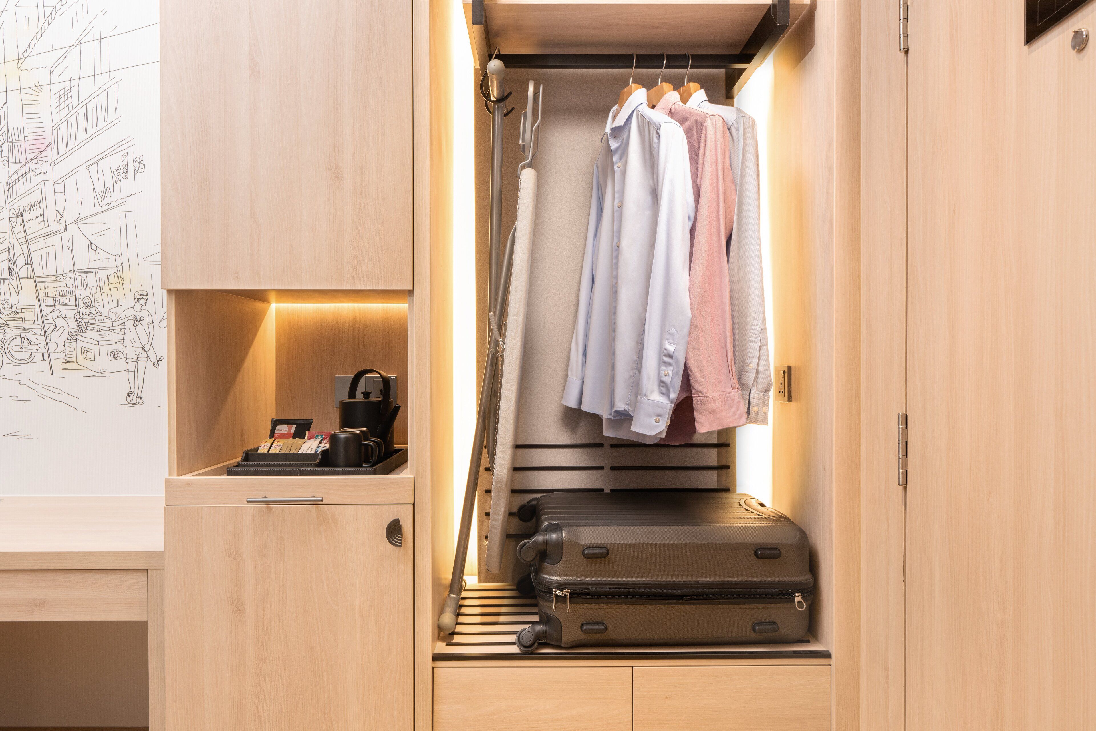 A compact room with a built-in wardrobe, a small desk with a coffee machine, and a hanging rack for clothes.