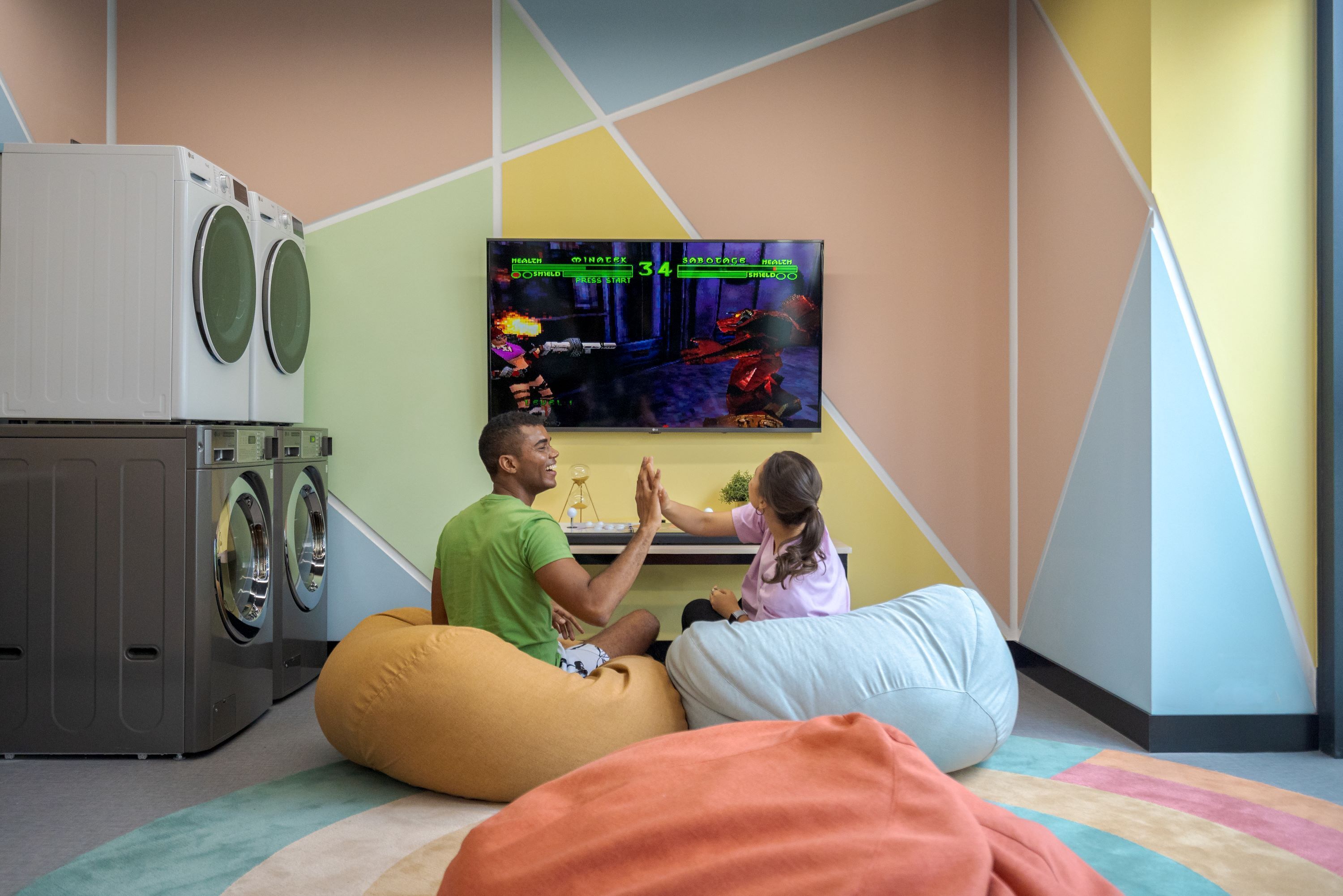 A room with a washing machine, a flat-screen TV displaying a video game, and two bean bags.