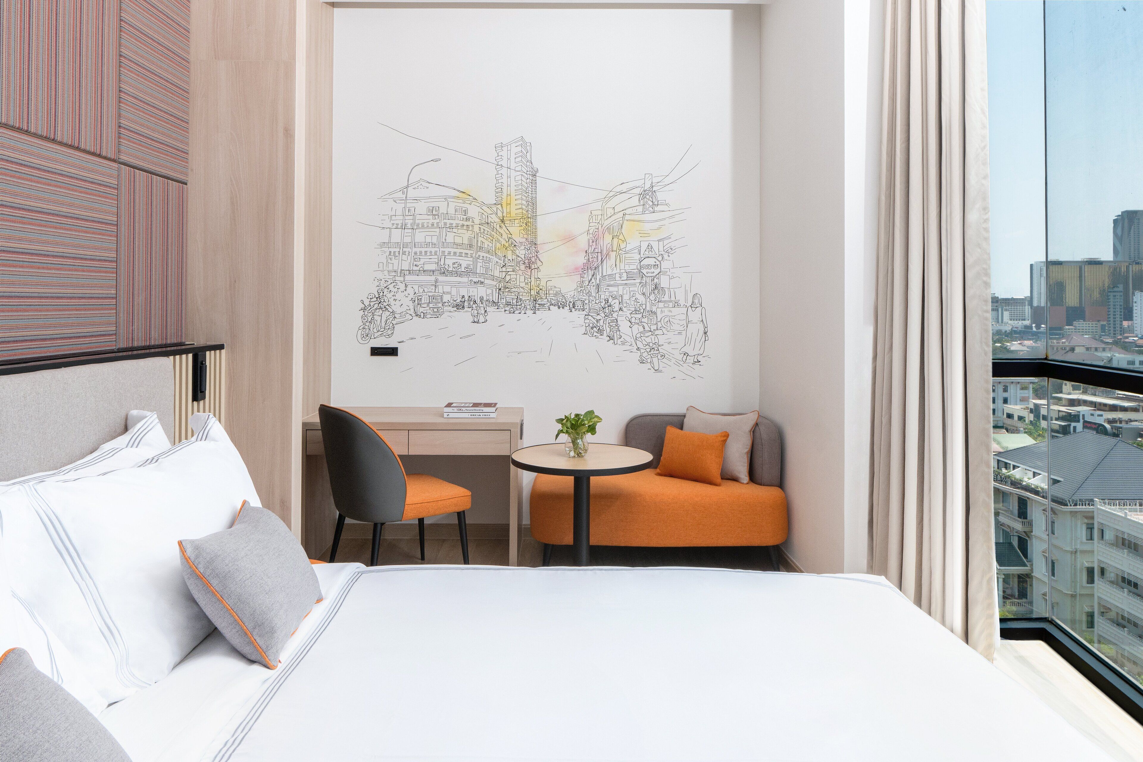 A hotel room with a large bed, a desk, a chair, a small table with a plant, and a cityscape view through the window.