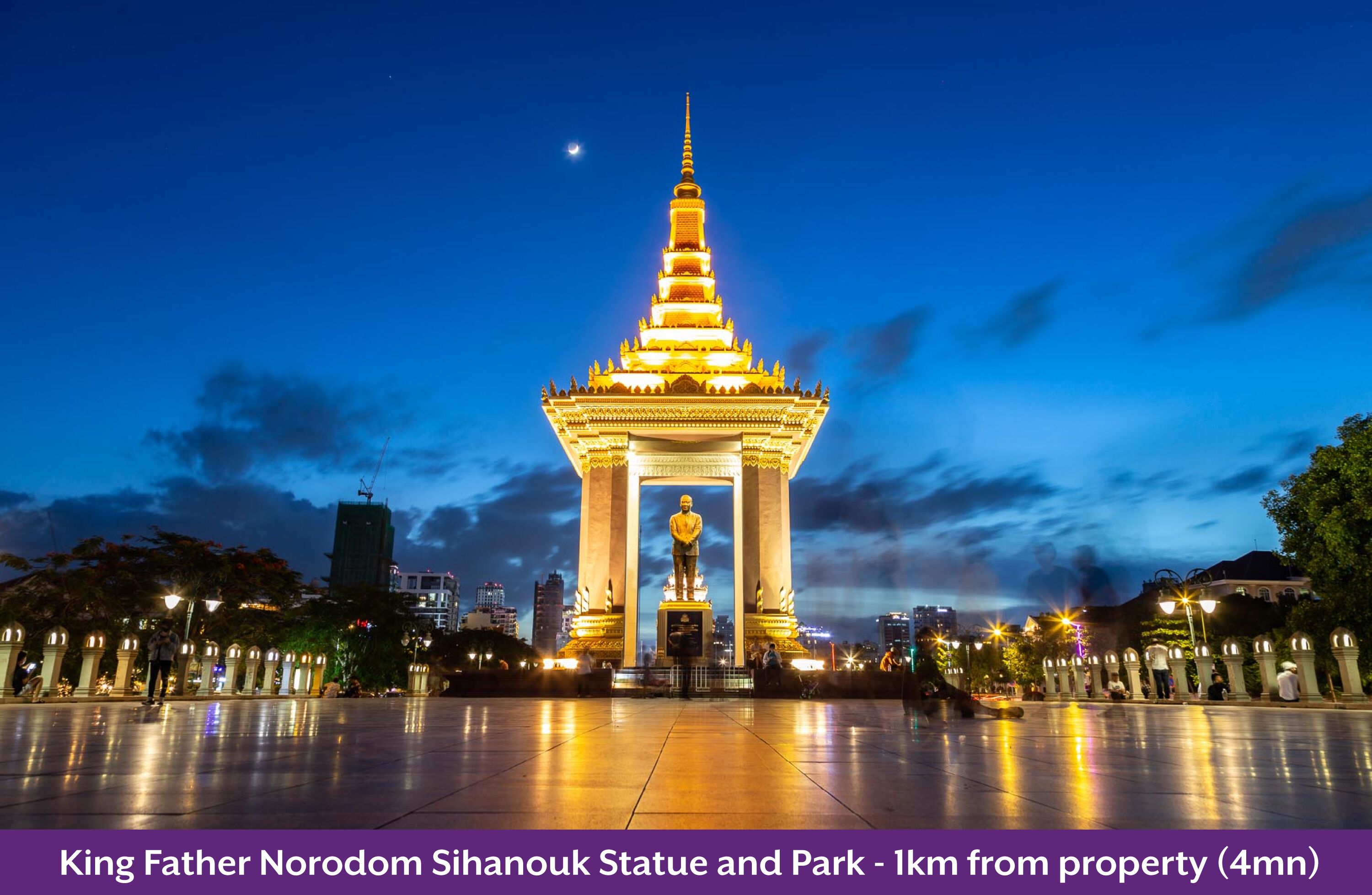 A nighttime view of the King Father Norodom Sihanouk Statue and Park, featuring a large illuminated statue and a spacious plaza.