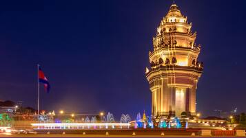 The Independence Monument at night, illuminated with lights and surrounded by a water fountain display.