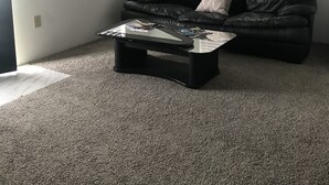 A living room with a black leather couch, a glass coffee table, and a ceiling fan.