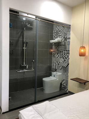 A modern bathroom with a glass-enclosed shower, a toilet, and a patterned wall. - Lacasa Homestay - Hostel (Hue)