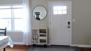 A room with a white door, a window with white curtains, a mirror on the wall, and a sign with a motivational quote.