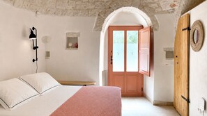 Un dormitorio con cama, lámpara de noche, puerta de madera y un estante con adornos.