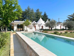 Une piscine bordée de pierres, un hamac et un bâtiment blanc doté de toits coniques.