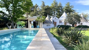 A swimming pool with a stone deck, surrounded by greenery and a covered seating area.