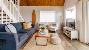 Ein Wohnzimmer mit Holzboden, einem blauen Sofa, einem weißen Sessel, einem Couchtisch mit einem Buch und einem Fernsehschrank.
