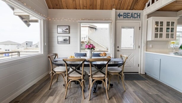 Ein Essbereich mit Holzbalkendecke, einem Tisch mit Stühlen, einer Tür mit der Aufschrift "BEACH" und Blick ins Freie.