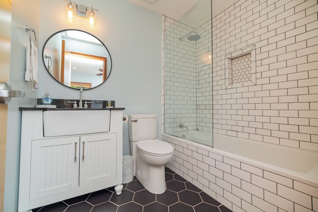 A bathroom with a white vanity, a round mirror, a toilet, and a glass-enclosed shower area.