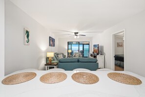 Una habitación moderna con ventilador de techo, un sofá, una mesa de comedor con individuales y vistas a través de un ventanal.