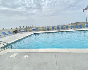 Relax by the pool with a clear view of the water, surrounded by lounge chairs and a flag.