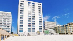 A beachfront hotel with multiple floors, a sandy beach in the foreground, and a clear blue sky. - Beach Front, Balcony access from den and master, Spacious living, fully equipped (Gulf Shores)