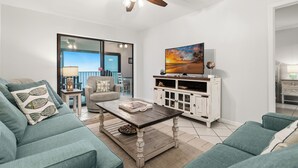 A living room with a sofa, coffee table, TV stand, and ceiling fan. - Beach Front, Balcony access from den and master, Spacious living, fully equipped (Gulf Shores)
