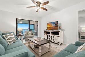 A living room with a sofa, coffee table, TV stand, and ceiling fan. - Beach Front, Balcony access from den and master, Spacious living, fully equipped (Gulf Shores)