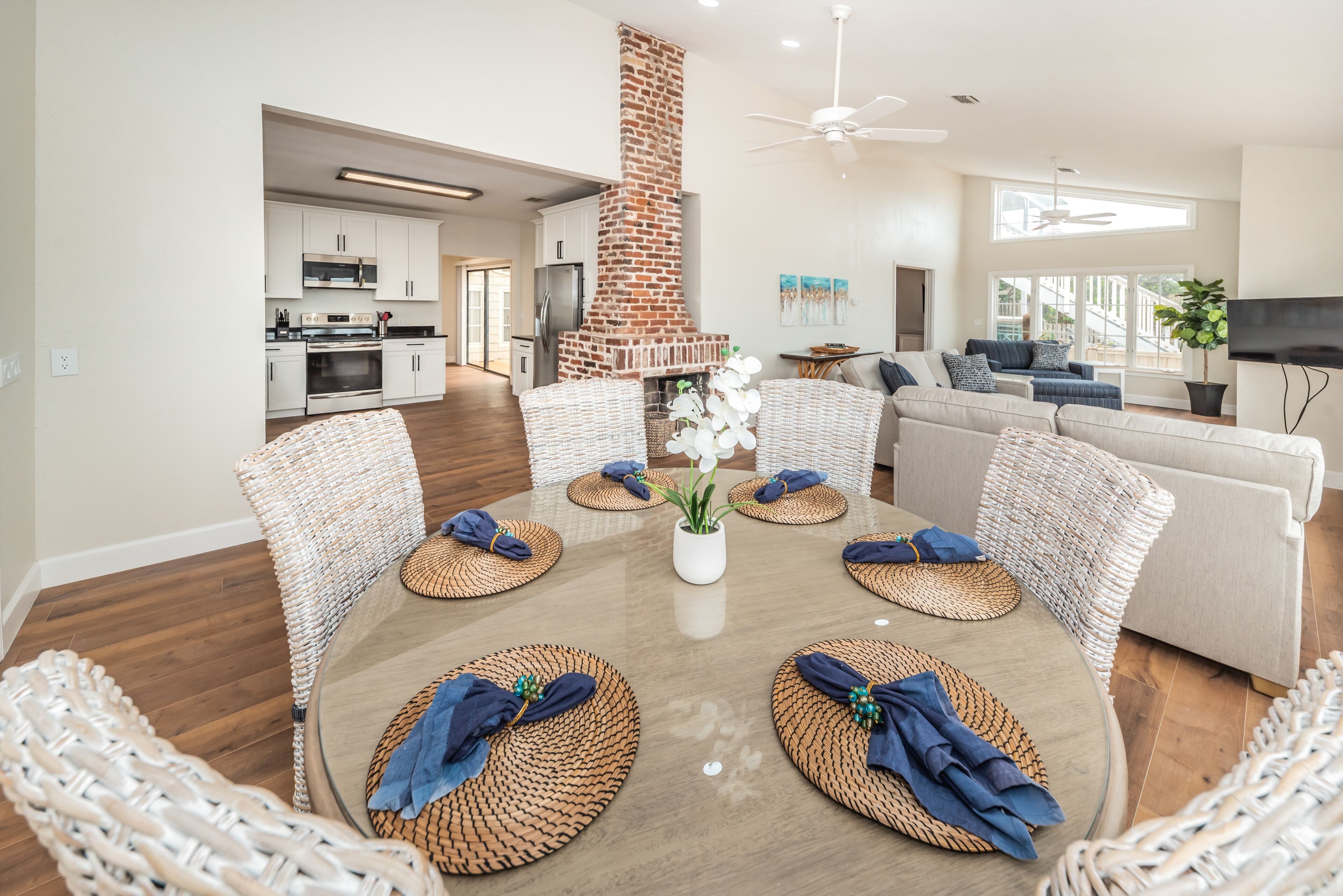 A modern living room with a central brick fireplace, wicker furniture, and a large TV.