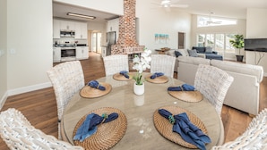 A modern living room with a central brick fireplace, wicker furniture, and a large TV. - Direct Oceanfront Oasis: Remodeled Home with Private Heated Pool (Indian Shores)