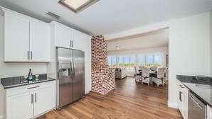 A modern kitchen with white cabinets, stainless steel appliances, and a brick fireplace. - Direct Oceanfront Oasis: Remodeled Home with Private Heated Pool (Indian Shores)