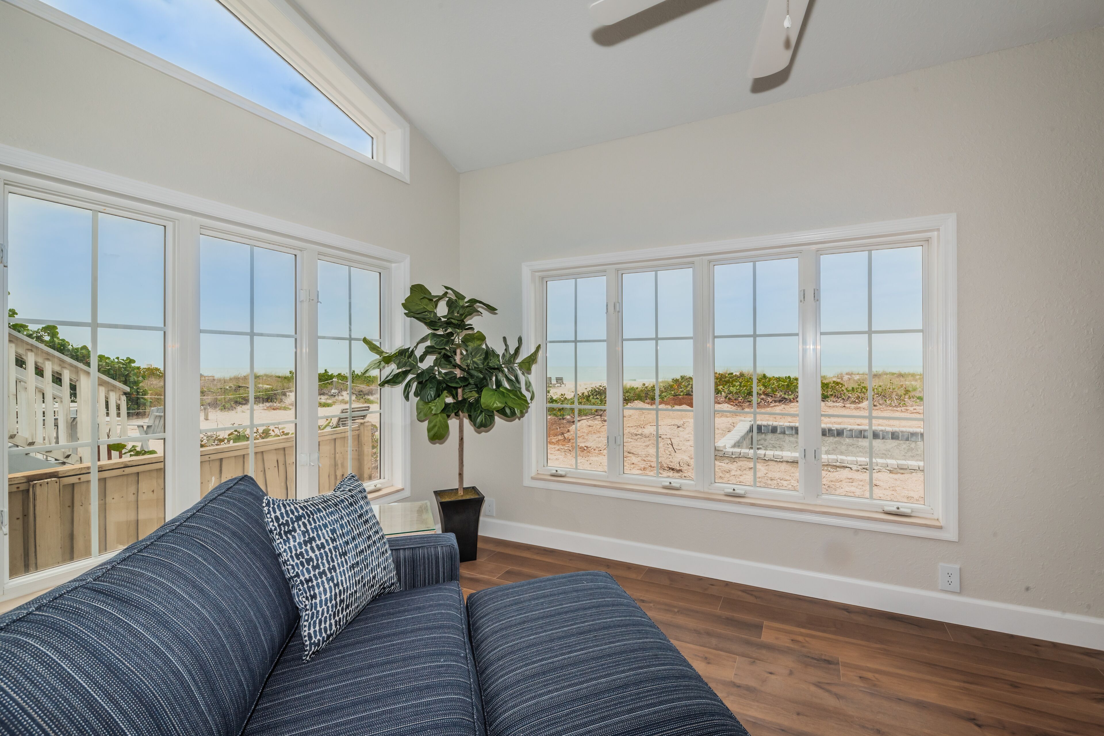 A spacious living room with large windows, a ceiling fan, and a potted plant.