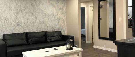 A living room with a black leather sofa, a white coffee table, and a large mirror on the wall.