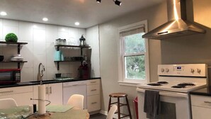 Una cocina moderna con armarios blancos, una campana extractora de acero inoxidable, un microondas y una estufa. Hay una ventana que proporciona luz natural y vistas al exterior.