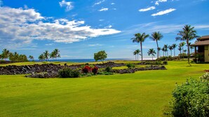 Un campo da golf con vista sull'oceano, palme e un edificio con un balcone.