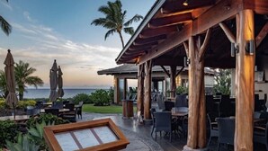 An outdoor seating area with tables and chairs, a wooden pergola, and a caution sign for a wet floor. - Paradise vibes awaits @ Hali"i Kai, ocean front resort in Waikoloa Beach (Waikoloa Village)