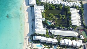Vista aerea di un resort con diversi edifici bianchi, una spiaggia e una zona piscina.