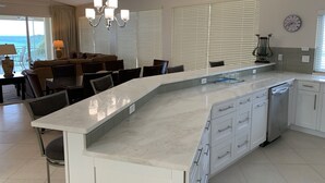 Una cucina moderna con un'isola grande, mobili bianchi e vista sull'oceano dalla zona pranzo.