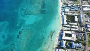 Vista aerea di una località balneare con diversi edifici alberghieri, una spiaggia e acque cristalline color turchese.
