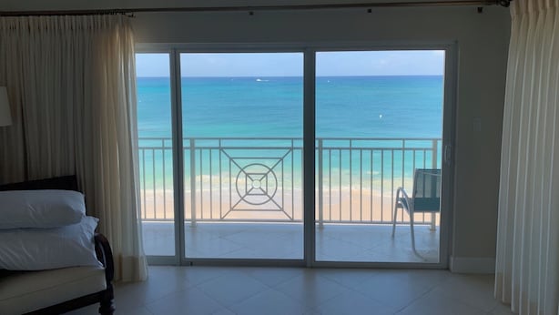 Una stanza con un letto, una sedia e vista sulla spiaggia e sull'oceano attraverso una porta finestra.