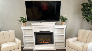 A living room with a fireplace, two armchairs, a television mounted above the fireplace, and two potted plants. - Sandusky 4 BR, 2-bath home. 3.5 Mi from Cedar Point. 3.2 Mi to Sports Force. (Sandusky)