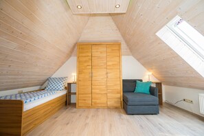 A room with a sloped ceiling, wooden walls, a bed with patterned bedding, a grey sofa with a teal pillow, and a wooden wardrobe. - Luxurious vacation apartment in a quiet, rural setting (Nordhalben)