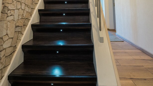 Una escalera con escalones de madera oscura y una pared de piedra a un lado.