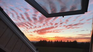 Un tragaluz con vista a una puesta de sol sobre un área boscosa.
