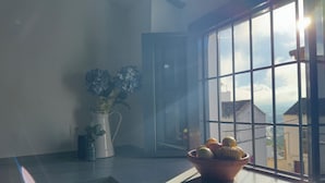 Een kamer met een groot raam, een vaas met bloemen en een schaal fruit op de vensterbank.