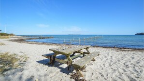 A sandy beach with a wooden picnic table and a pier extending into the water. - 3 bedroom stunning home in Hejls (Hejls)
