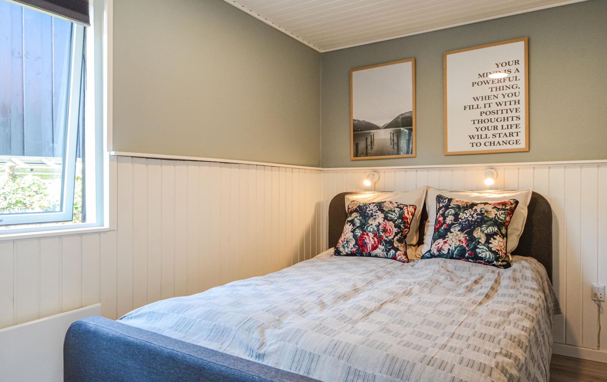 A bedroom with a bed, two wall-mounted light fixtures, and two framed motivational quotes.