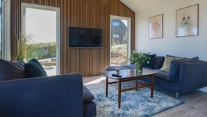 A modern living room with a large TV, comfortable seating, and a view of the outdoors. - 3 bedroom stunning home in Hejls (Hejls)