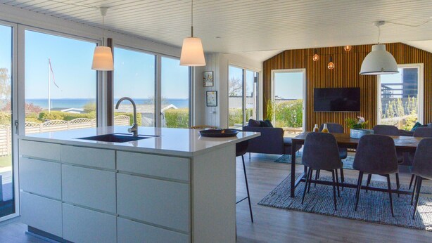 A modern kitchen with a large island, a dining area with a TV, and a view of the ocean. - 3 bedroom stunning home in Hejls (Hejls)