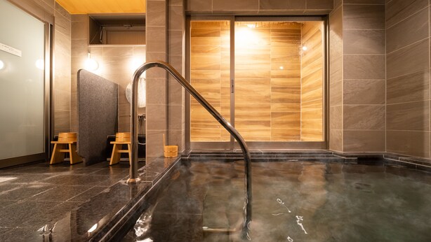 A modern spa with a heated stone bath, wooden stools, and a wooden partition wall. - SuperHotel Yahaba-Eki Higashiguchi (Yahaba)