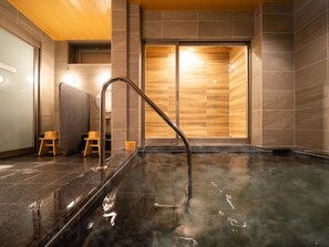 Un spa moderne doté d’un bain en pierre chauffé, de tabourets en bois et d’une cloison en bois.