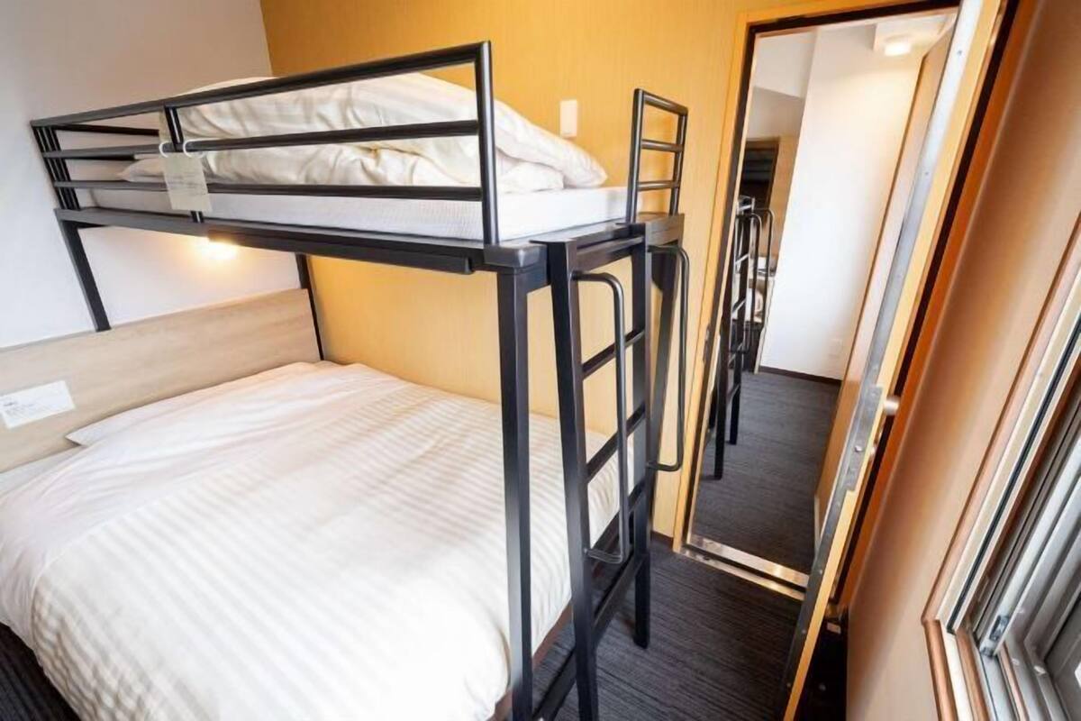 Una cama litera con escalera, una cama individual abajo, un espejo y una puerta que da a otra habitación.