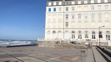 Een groot, meerhoog gebouw met een symmetrische gevel, een opvallende ingang met treden en een uitzicht op zee op de achtergrond.
