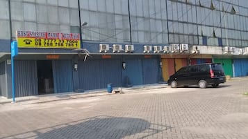 Um edifício com uma placa indicando 'KOST STARIHA MAMA @ KUTA JAYA' e um carro preto estacionado em frente.