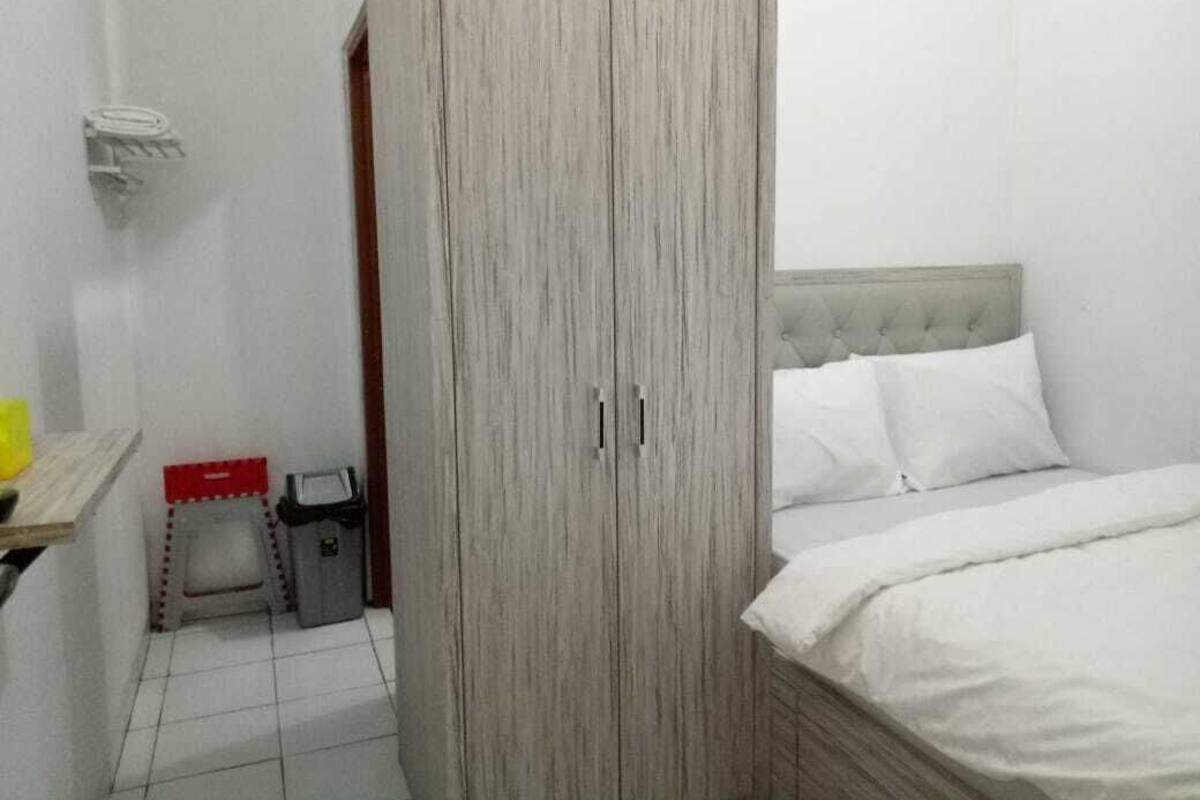 A bedroom with a bed, a wardrobe, a small stool, and a trash bin.