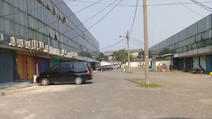 A paved street with buildings on either side, a black car parked on the left, and a motorcycle on the right. - Hotel Syariah Mama Kutajaya Pasar Kemis (PasarKemis)